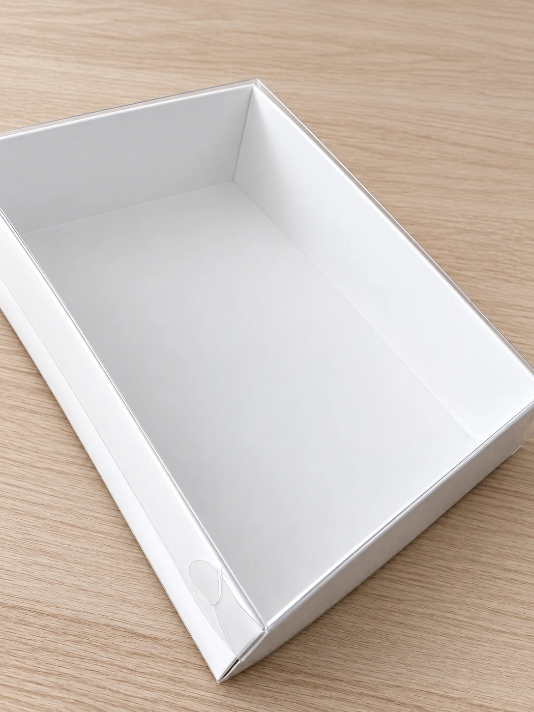 Empty white Premium Gloss Suit Box with its clear lid, shown assembled on a wooden surface